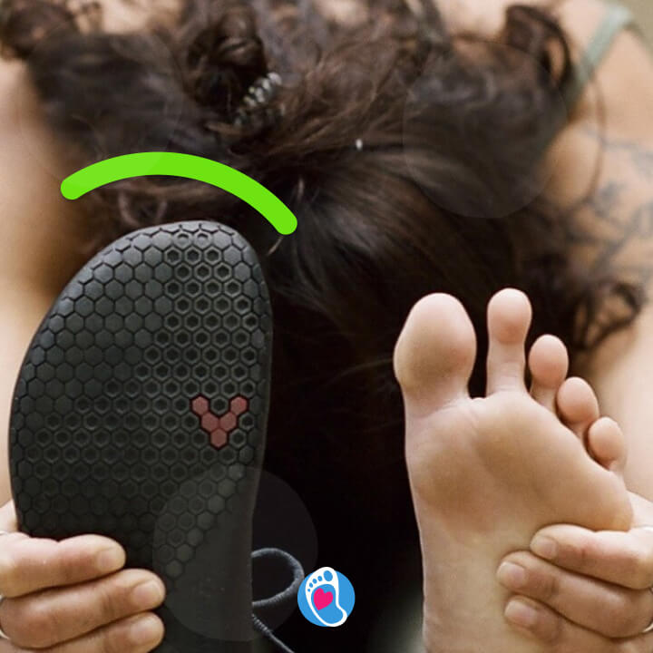 Kobieta wykonuje skłon z wyprostowanymi nogami, trzyma dłońmi stopy, jedna bosa, druga w bucie barefoot - vivobarefoot