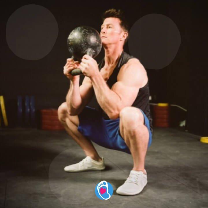 Mężczyzna ćwiczy w butach barefoot z kettlami w pozycji kucania - vivobarefoot