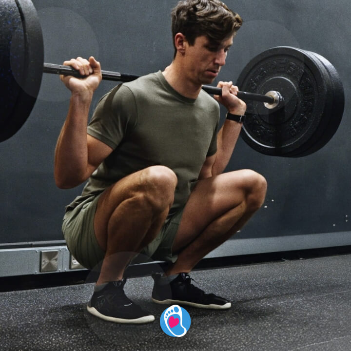 Mezczyzna w przysiadzie ze sztanga, trenujacy w butach barefoot barefoot - Vivobarefoot na silowni.