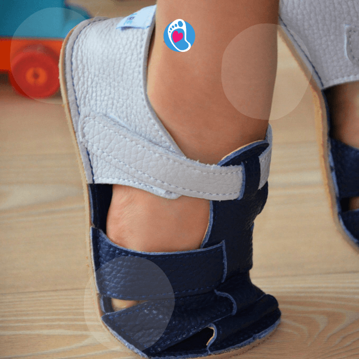 baby-bare-buty-barefoot-sandalki-granatowe-na-nodze-dziecka-wnetrze-Bosa-Stopka Granatowo szare sandałki barefoot Baby Bare w domowym wnętrzu. Naturalny ruch i wygoda dla stópek dziecka.