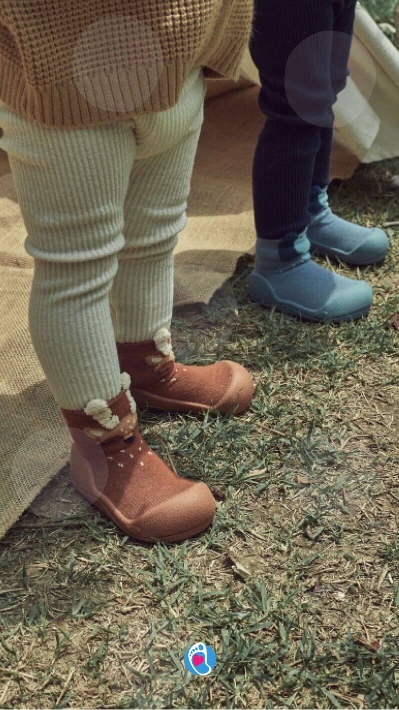 Attipas–buciki-barefoot-dla-dzieci-do-zabawy-na-swiezym-powietrzu Dzieci w bucikach barefoot Attipas stojące na trawie podczas zabawy na zewnątrz