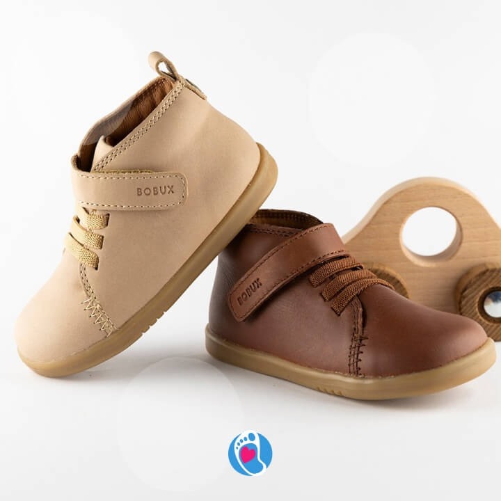 bobux-iWack-Voyager-buty-barefoot-buty-dzieciece-elastyczne-dwa-kolory-wozek-Bosa-Stopka Buty barefoot Bobux iWack Voyager w odcieniach bezowym i brazowym obok drewnianej zabawki. Idealne buty do nauki chodzenia, elastyczne i anatomiczne.